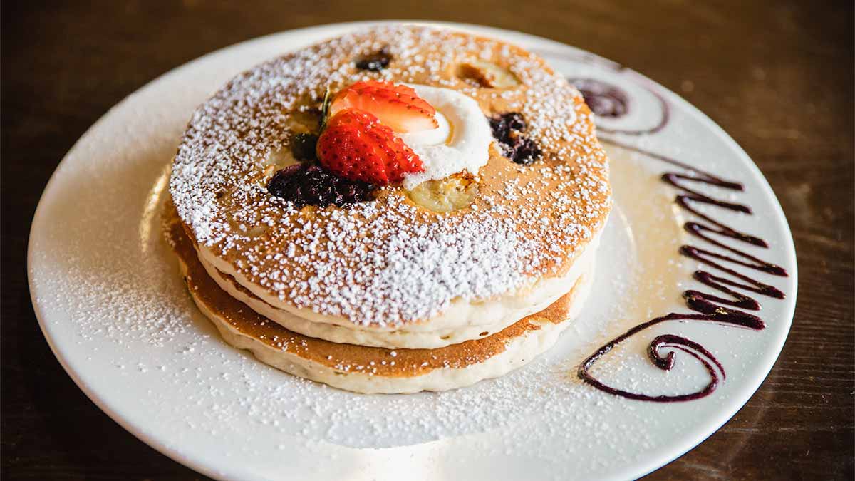 close up of plate of pancakes with strawberries, powdered sugar, cream, and chocolate sauce on the side at The Mission - San Diego, California, USA